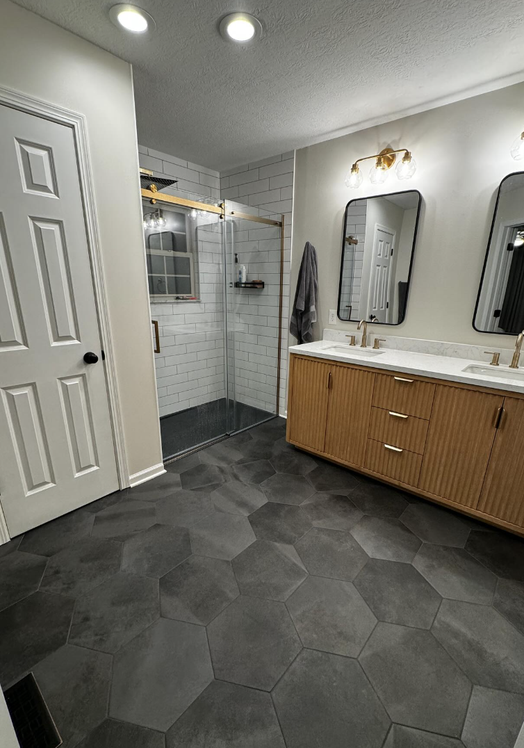 Finished primary bathroom with gold fixtures, hex tile floor, and subway tile shower